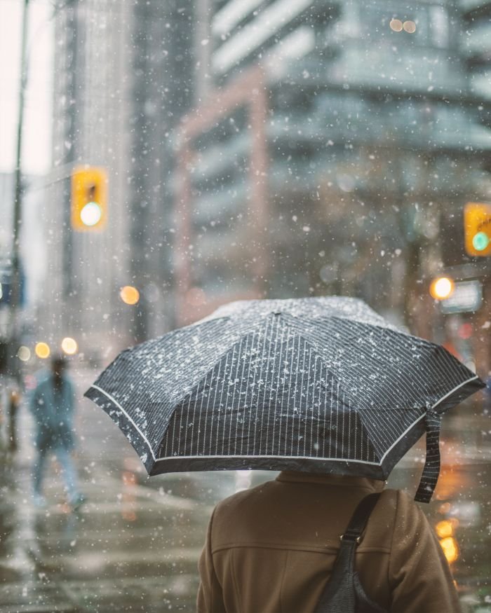 services-04 A person with an umbrella walks in a snow-covered urban street, creating a serene winter atmosphere.